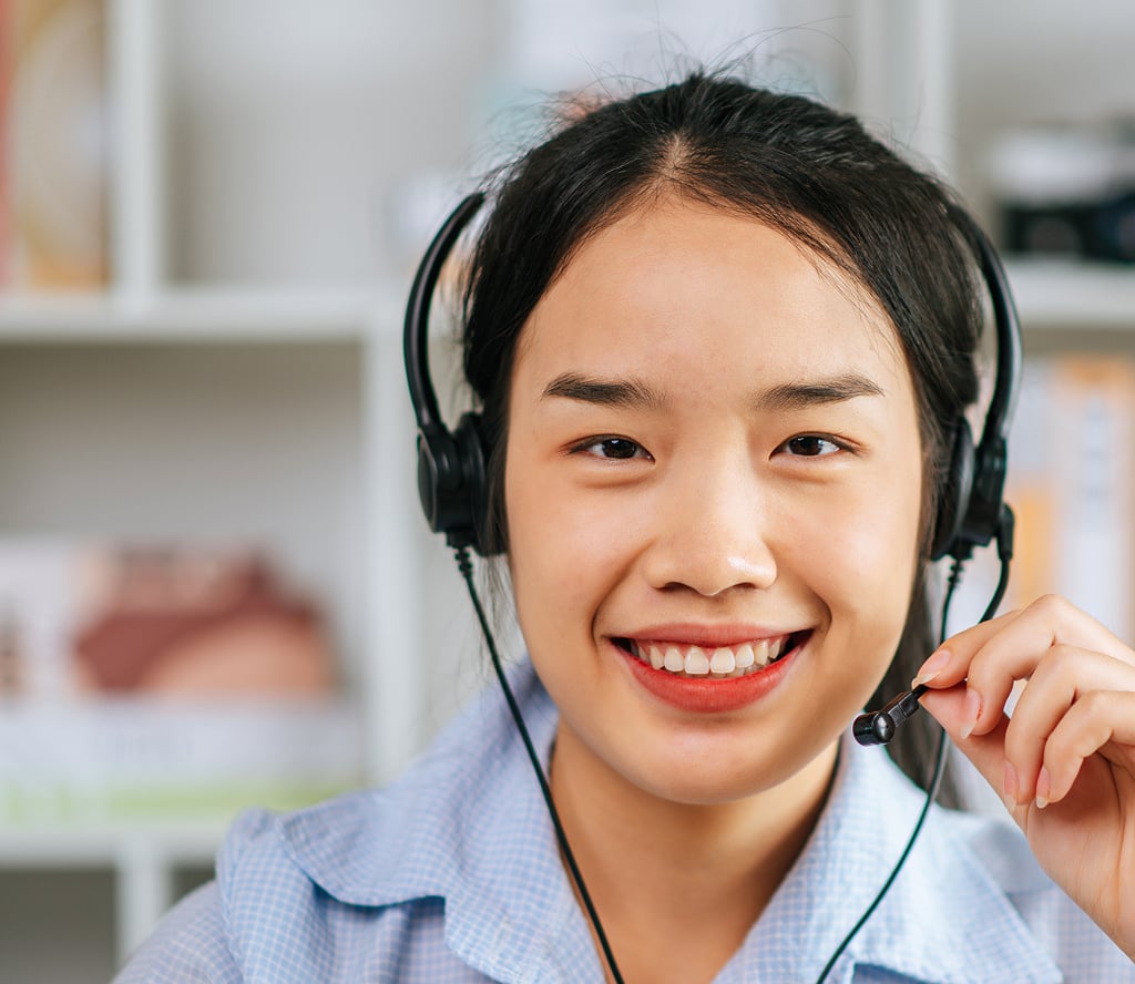 Cheerful Asian woman with headset smiling during a video conference call on her laptop