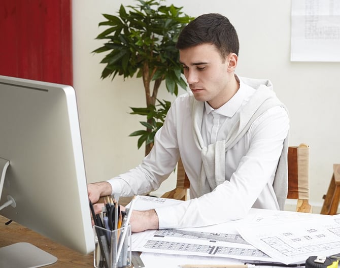 Male architect reviewing project drawings and working on a CAD system at his desk