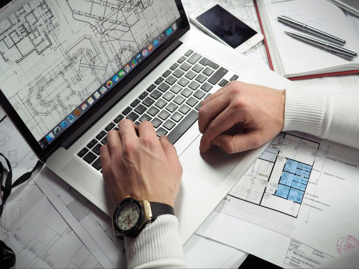 Designer reviewing architectural CAD drawings on a laptop surrounded by printed plans