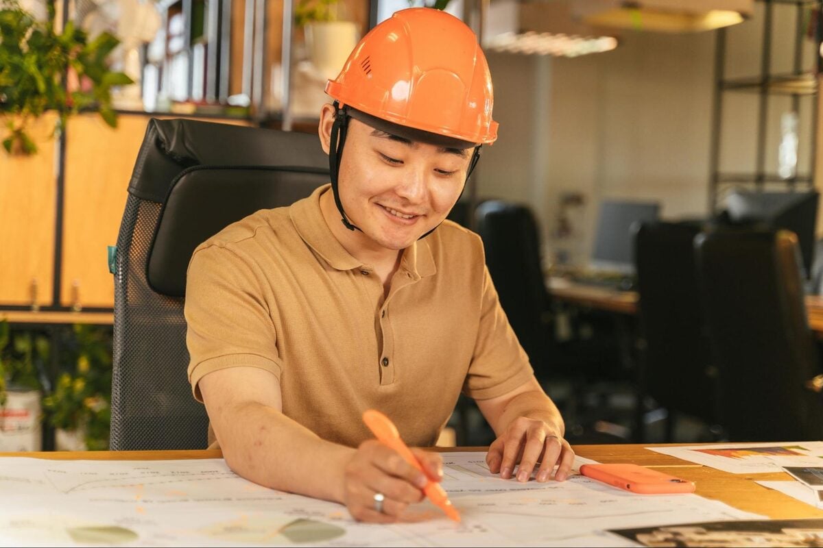 Smiling construction estimator in a hard hat marking up documents at a desk