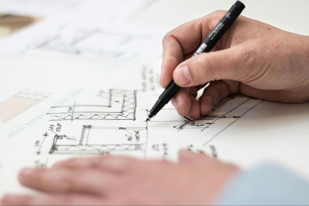 Engineer sketching structural construction details with a pen on technical drawings
