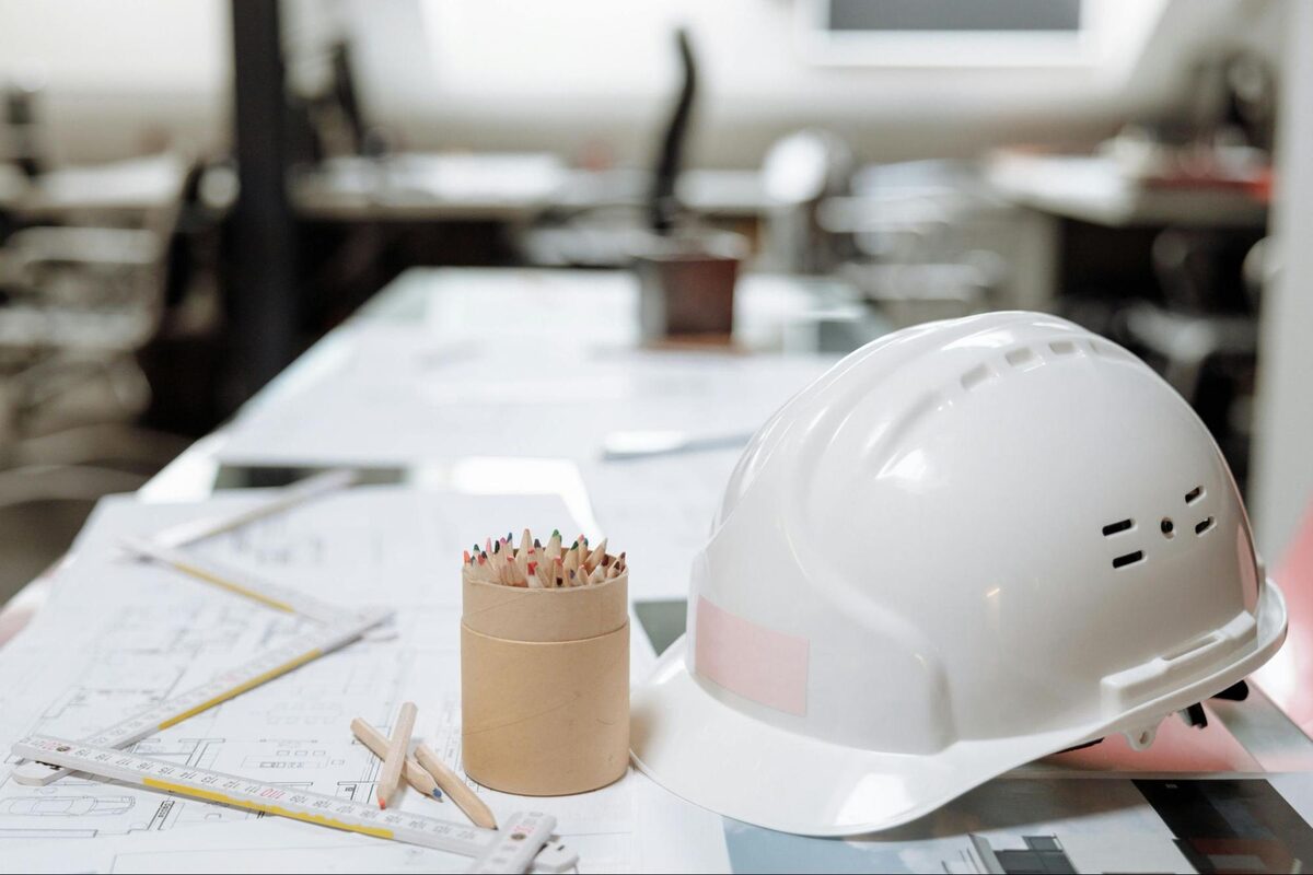 White hard hat and coloured pencils resting on architectural blueprints in an office