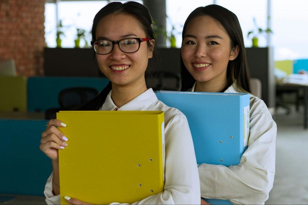Two smiling offshore administrative staff holding document binders in an office