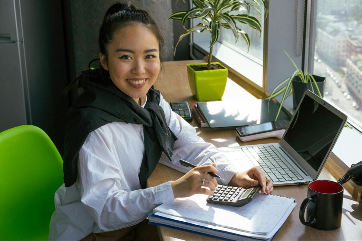 Smiling offshore bookkeeper working with a calculator and notebook at a desk