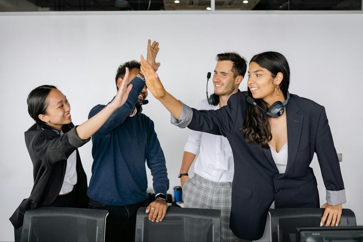 Diverse offshore team members wearing headsets celebrating with high fives in an office