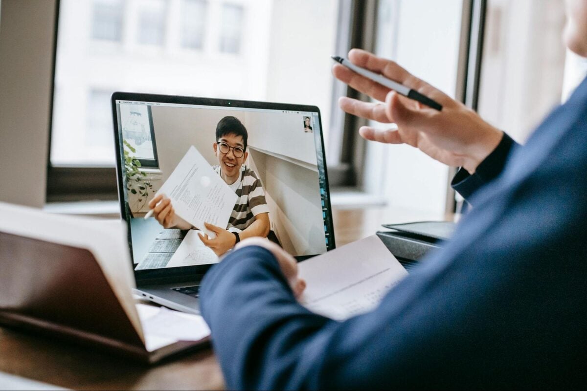 Manager on a laptop video call with a remote offshore candidate holding a document