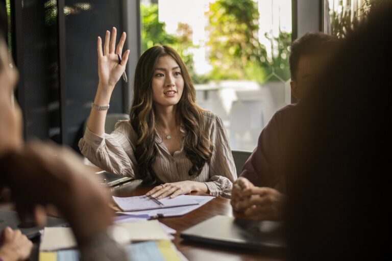 Businesswoman raising her hand to ask a question in a meeting, representing the questions to ask when choosing an offshore partner